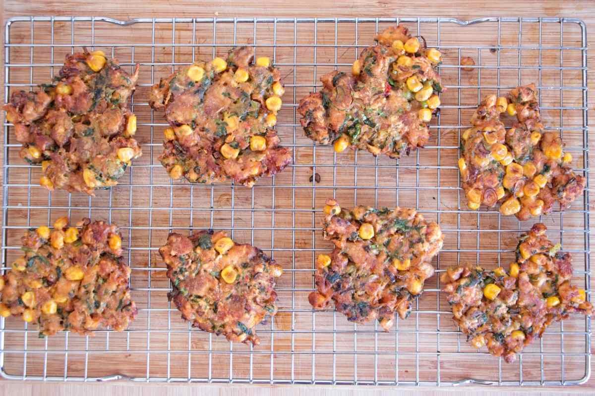 Freshly fried fritters cooling on a wire rack after frying, showing crisp edges and sweetcorn throughout.