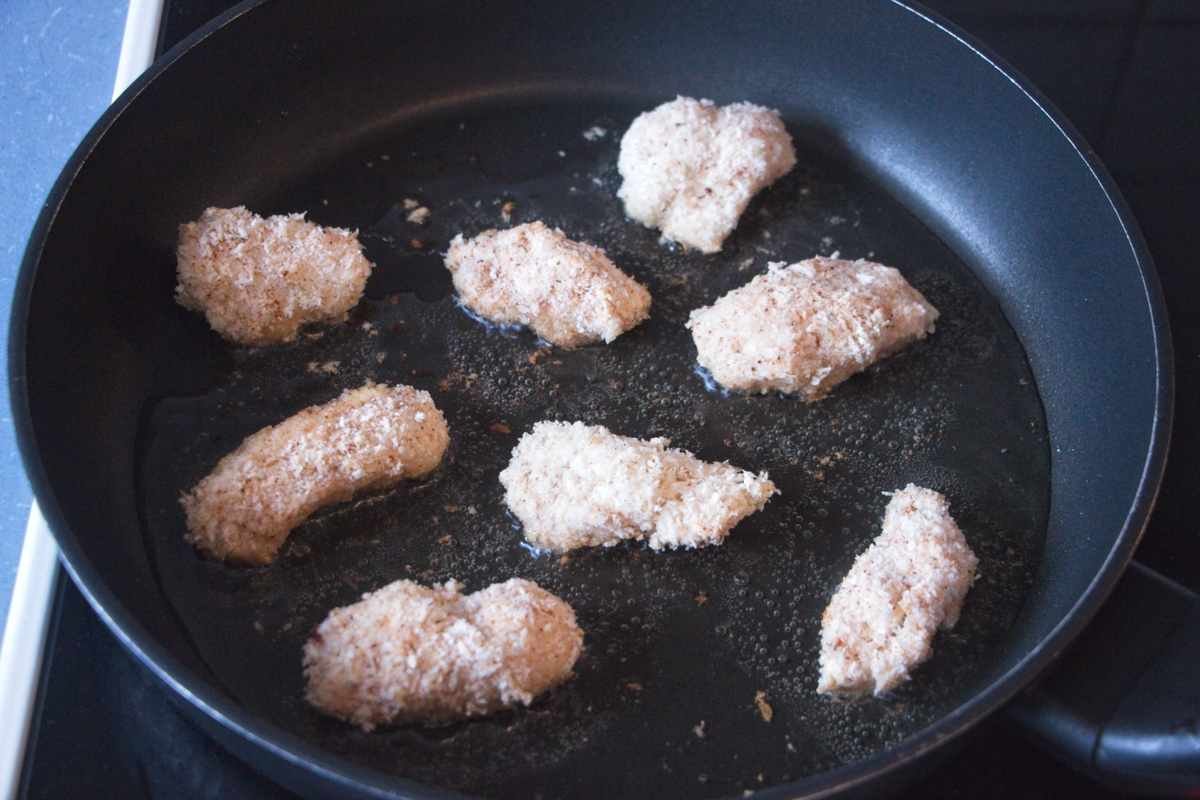 Breaded lion’s mane mushroom nuggets frying in a shallow layer of oil in a nonstick pan.