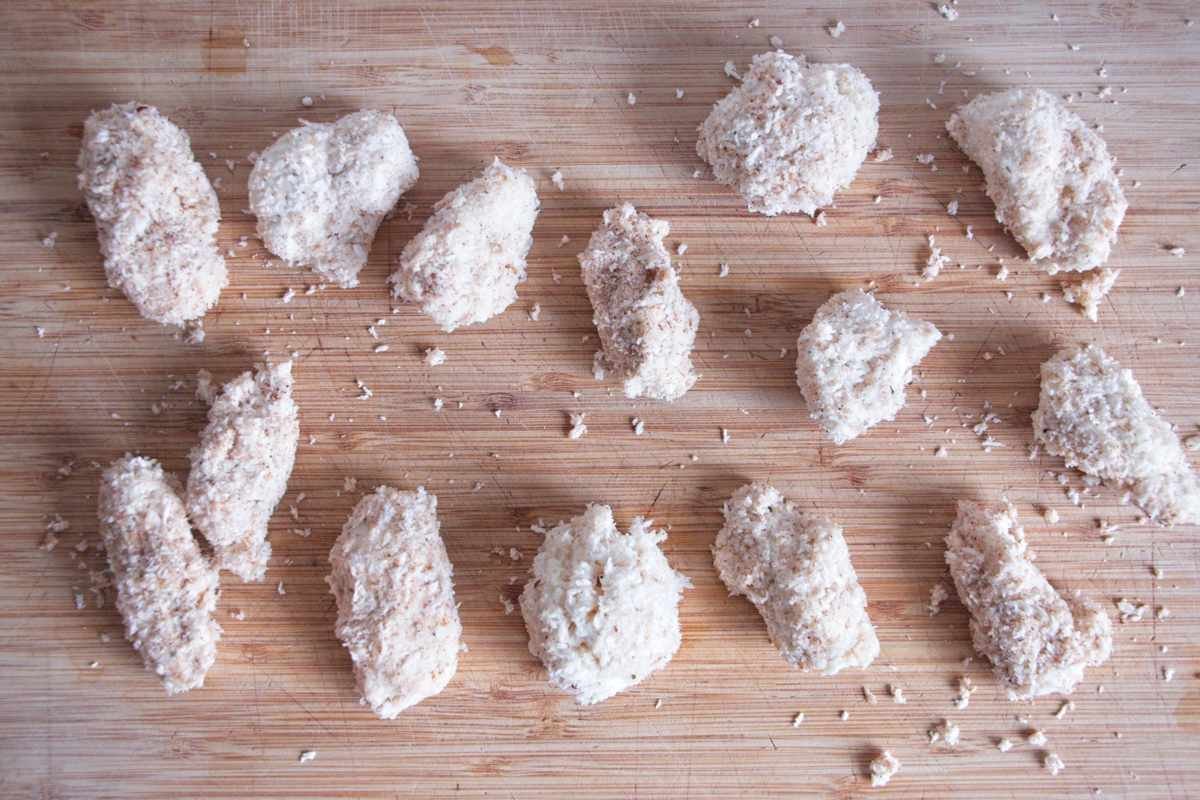 Mushroom pieces coated evenly in seasoned panko breadcrumbs on a wooden board before frying.