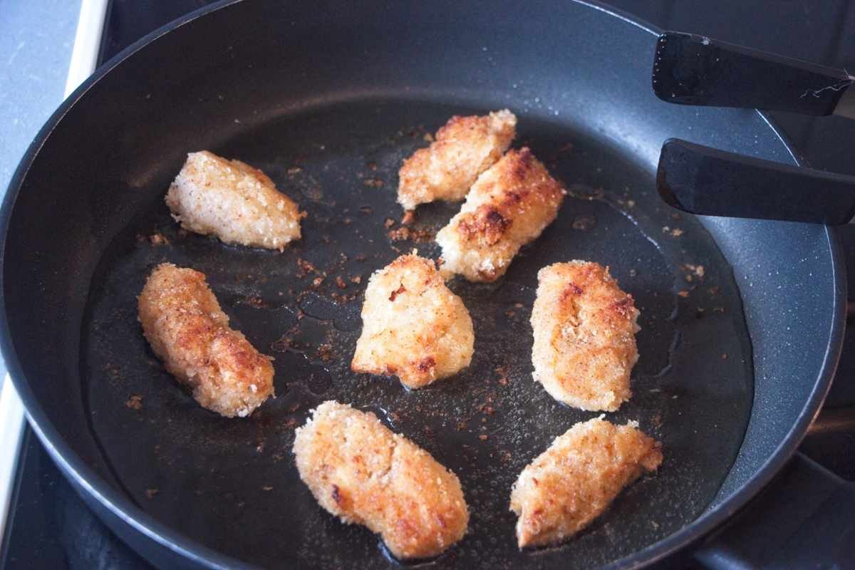 Breaded mushroom pieces shallow frying in a pan until deep golden and crisp on the outside.
