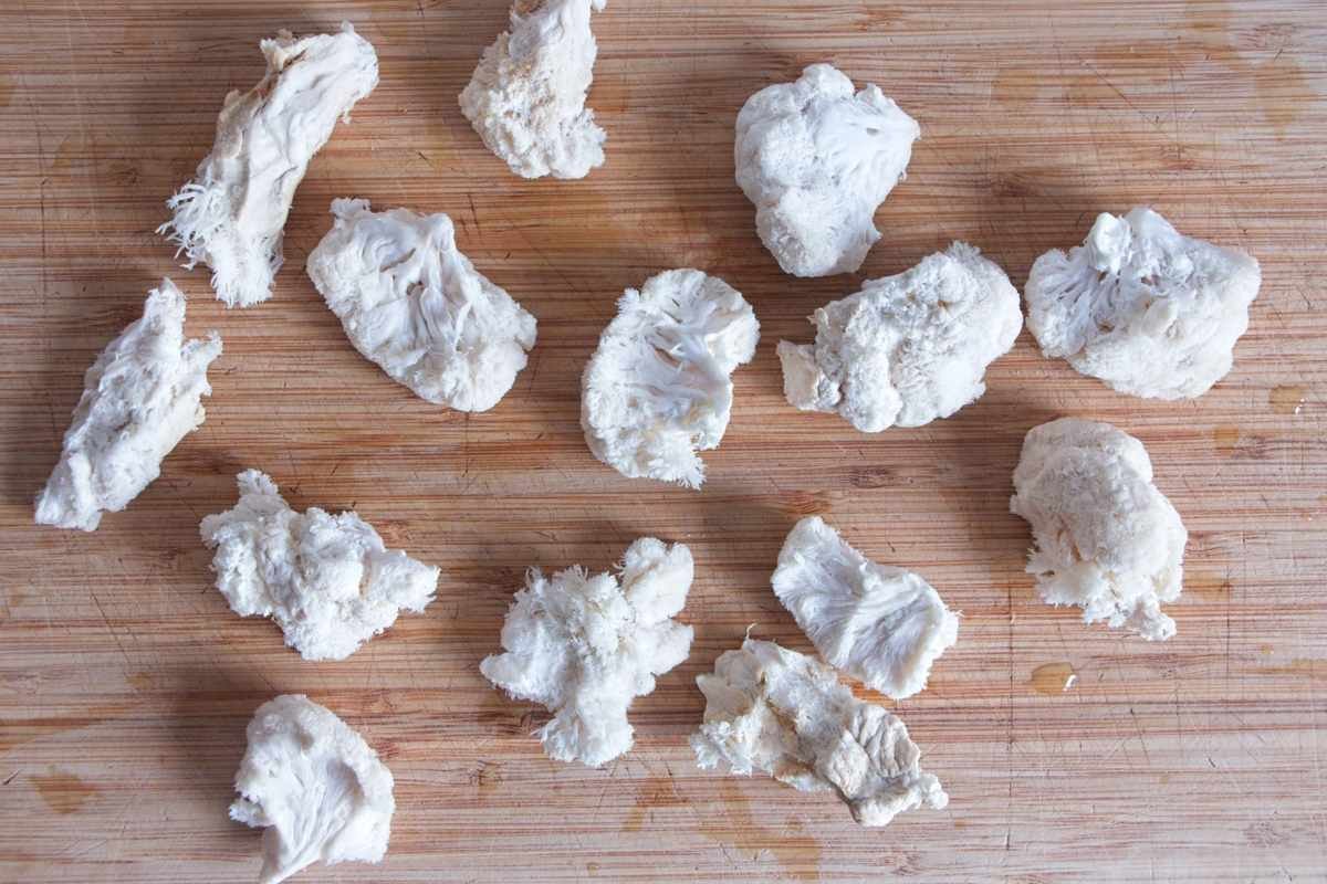 Torn lion’s mane mushroom pieces on a wooden board after excess moisture has been squeezed out.