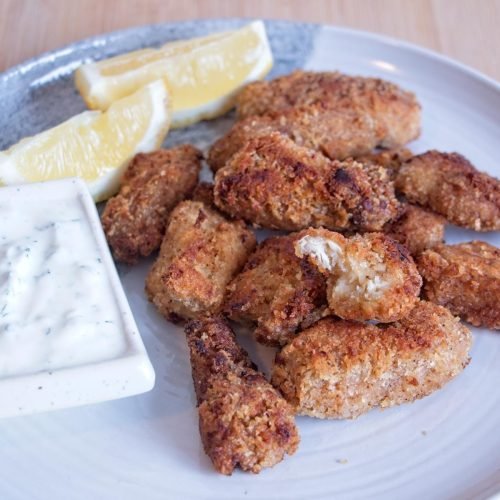 Lion’s mane mushroom nuggets served on a plate with creamy herb dip and lemon wedges, golden and crisp on the outside.
