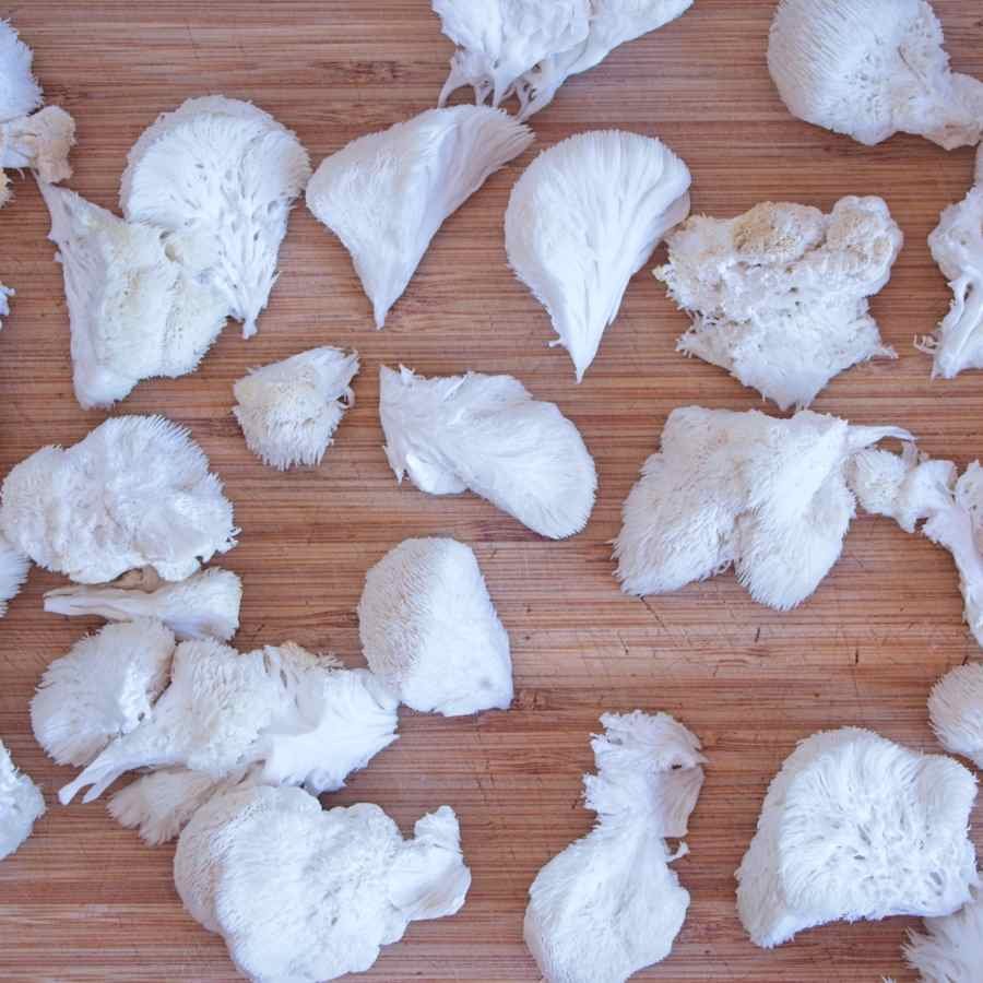 Torn pieces of fresh lion’s mane mushroom spread out on a wooden chopping board.