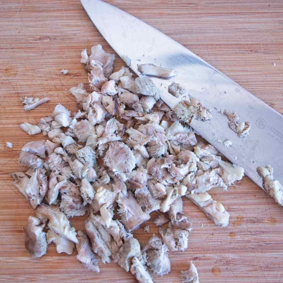 Roughly chopped lion’s mane mushroom on a wooden board with a chef’s knife.