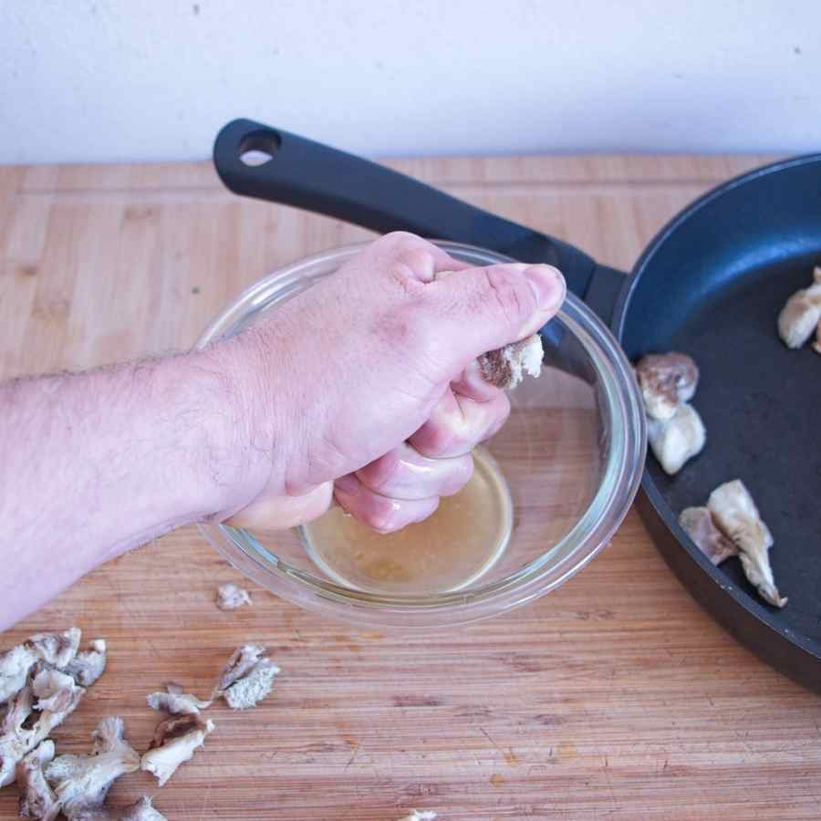 Hand squeezing excess liquid from cooked lion’s mane mushroom over a bowl before mixing into fritter batter.