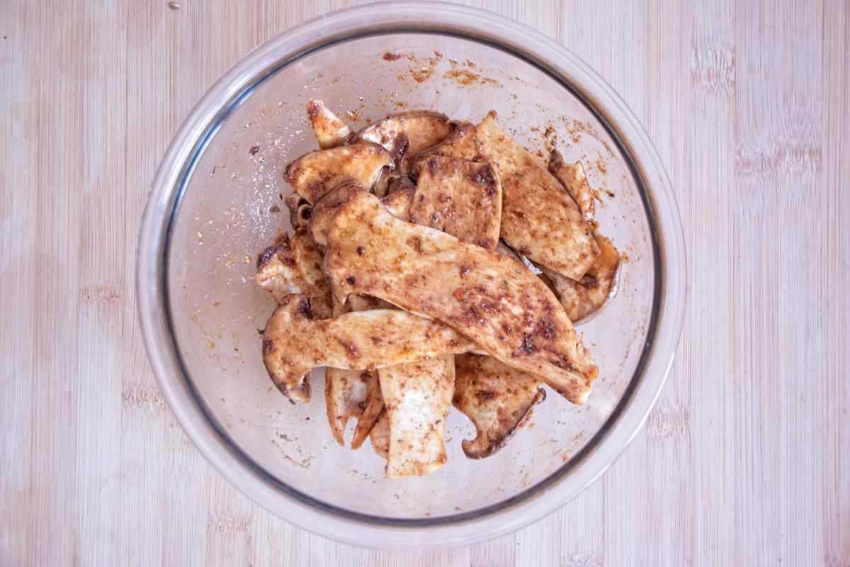 King oyster mushroom slices coated in smoky marinade in a glass bowl before baking.