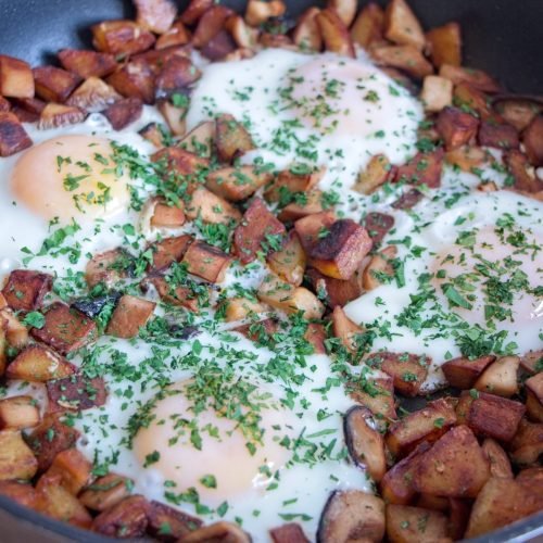 Close-up of king oyster mushroom breakfast hash with golden potatoes and soft eggs topped with chopped herbs.