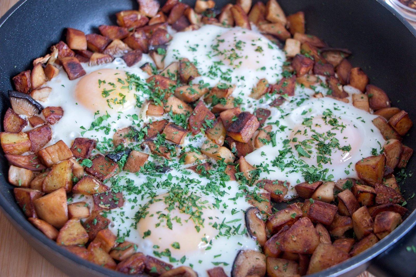 Close-up of king oyster mushroom breakfast hash with golden potatoes and soft eggs topped with chopped herbs.