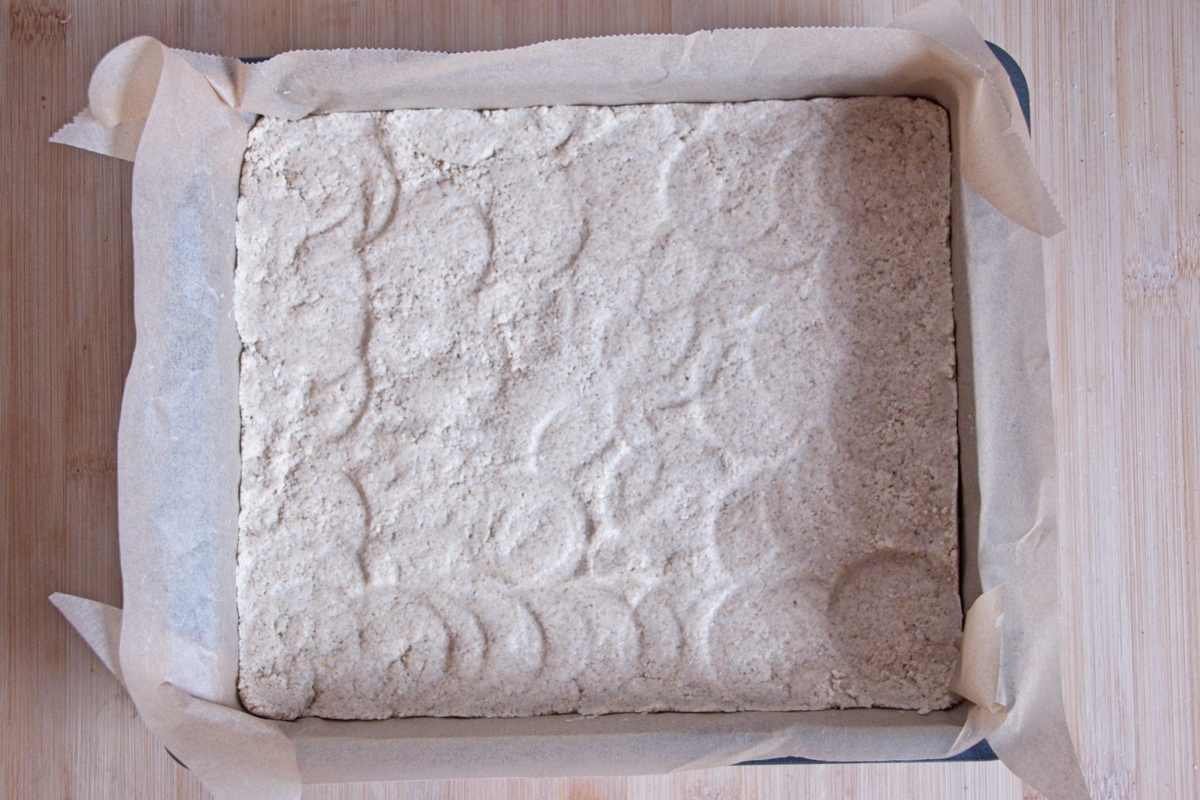 Pressed oat shortbread base evenly compacted in a lined square tin before chilling