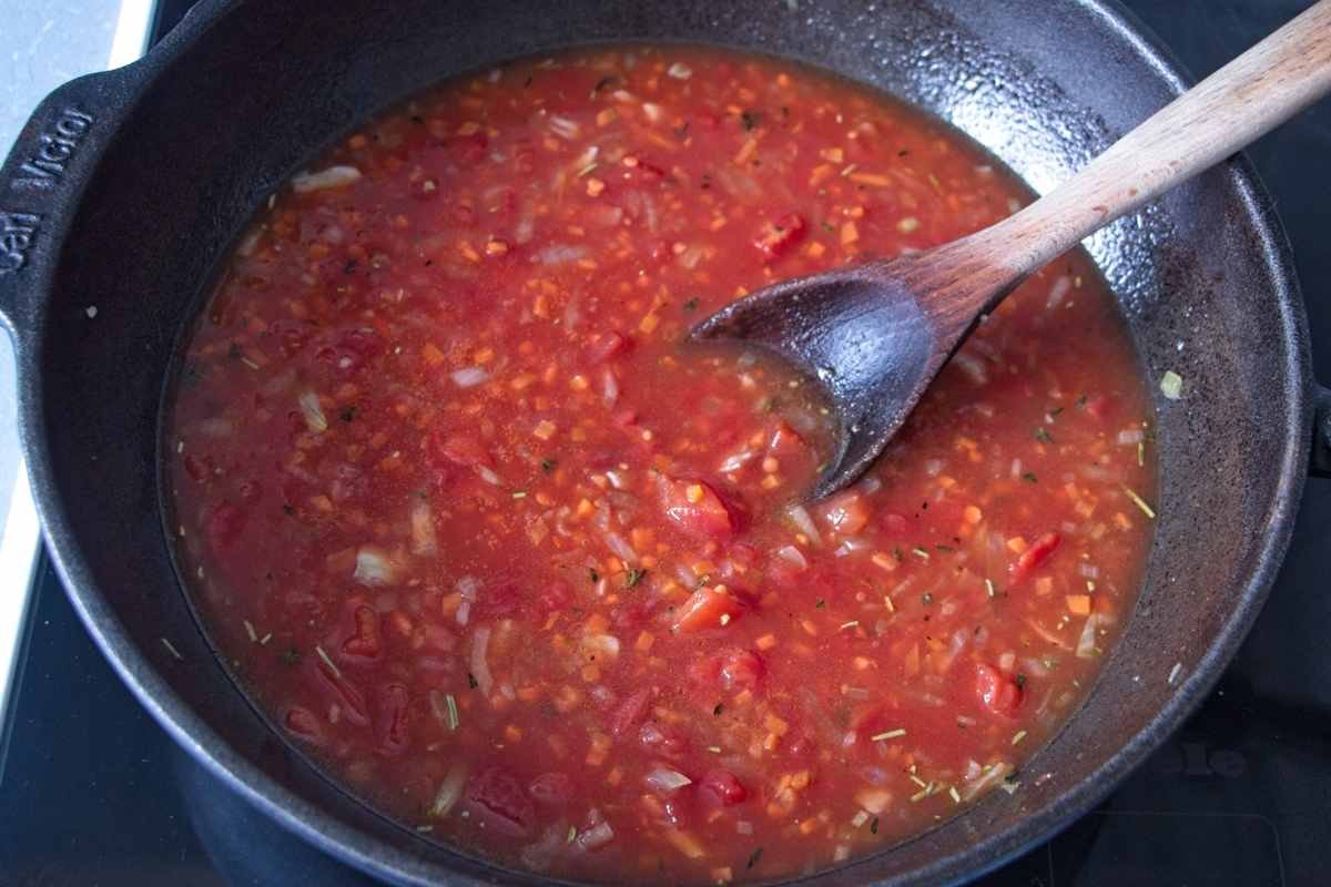 Chopped tomatoes and herbs added to the pan with sautéed vegetables, beginning to form the sauce base.