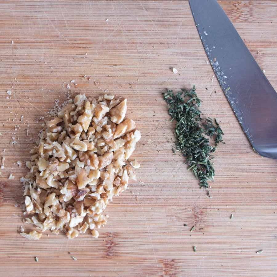 Finely chopped walnuts and fresh thyme on a wooden board beside a chef’s knife, ready to add to the sauce.