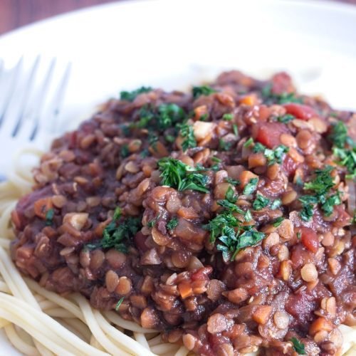 Close-up of red lentil walnut ragu spooned over spaghetti, showing the thick tomato sauce and chopped parsley garnish.