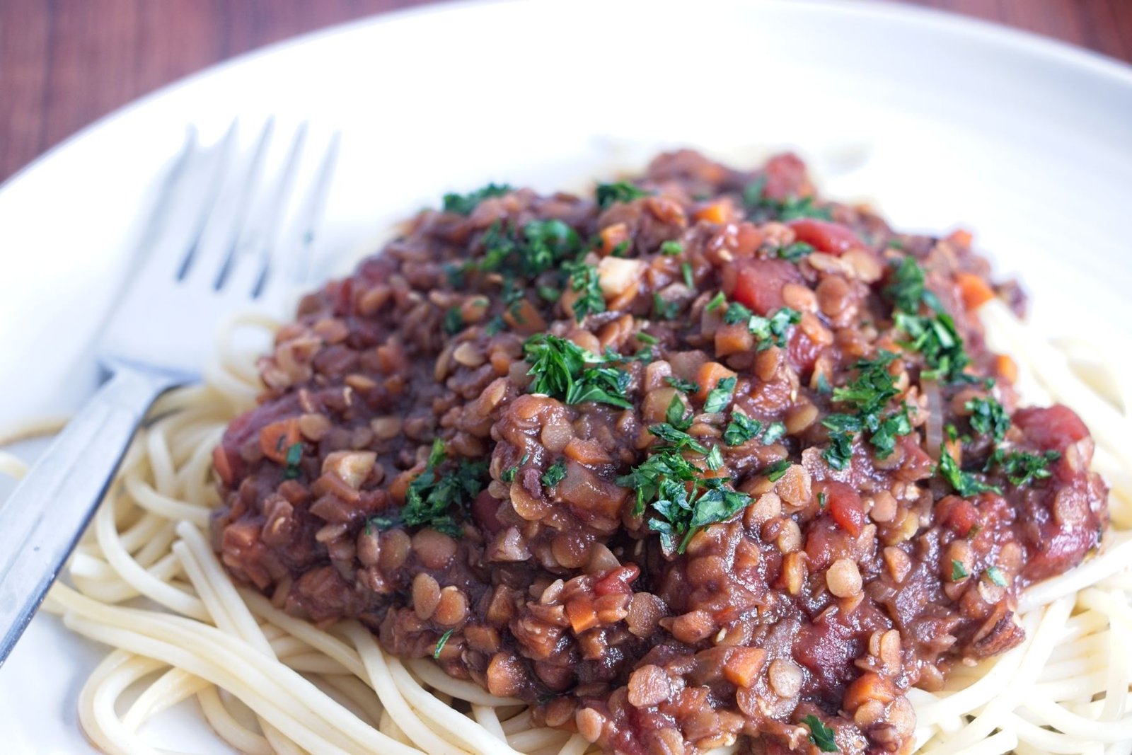 Close-up of red lentil walnut ragu spooned over spaghetti, showing the thick tomato sauce and chopped parsley garnish.