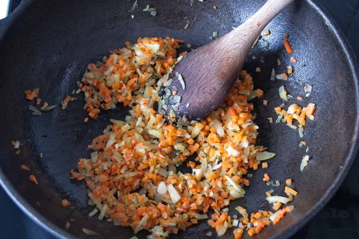 Finely diced onion and carrot cooking in a pan with a wooden spoon until softened and lightly golden.