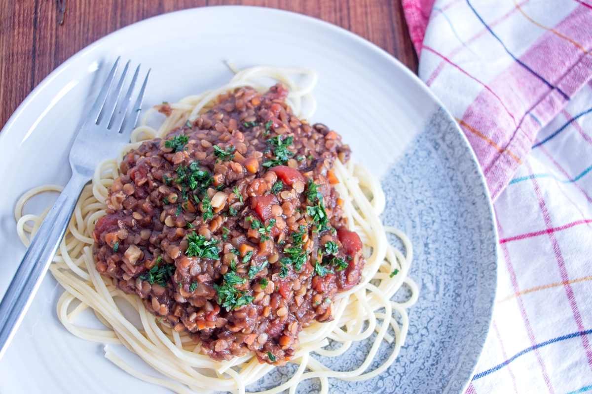 Red lentil walnut ragu spooned over spaghetti and finished with chopped parsley on a white plate.