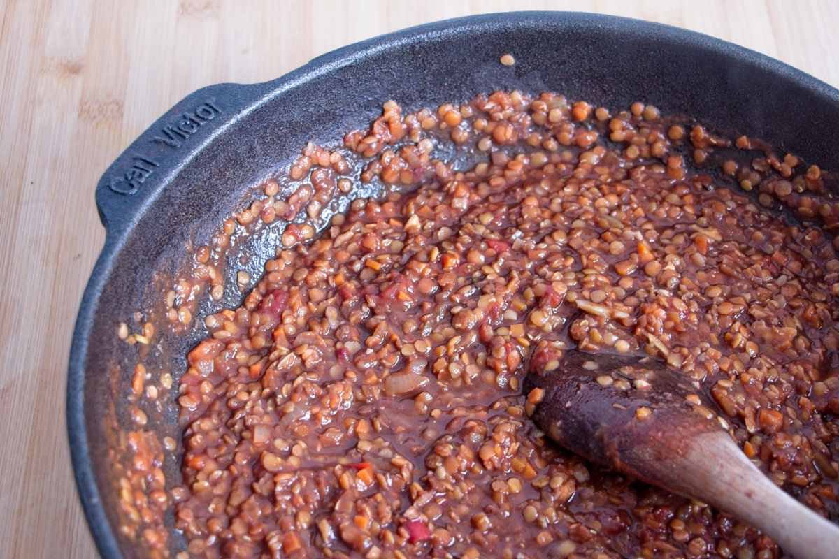 Red lentil walnut ragu thickening in a cast iron pan, showing soft lentils and finely chopped walnuts in a rich tomato sauce.