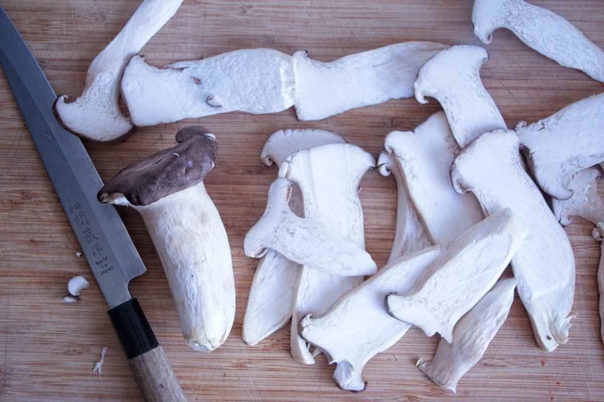 Sliced king oyster mushrooms arranged on a wooden board with a knife, ready for marinating.