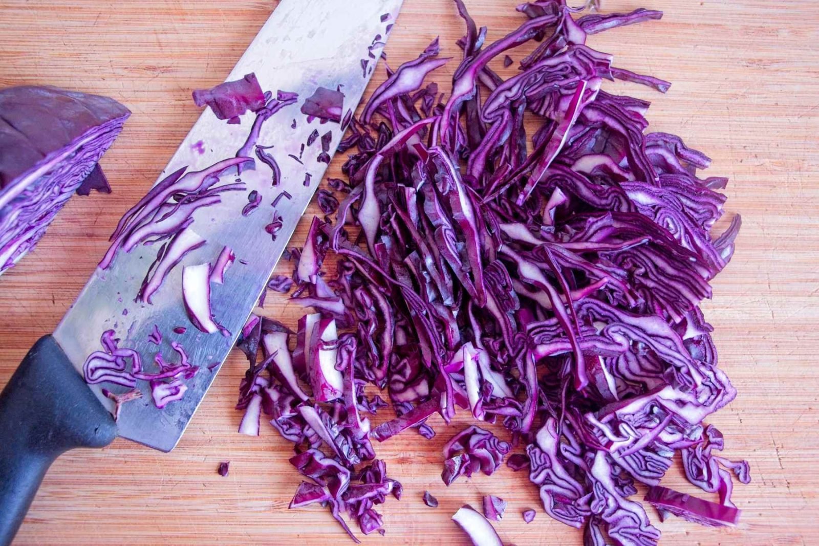 Thinly sliced red cabbage on a chopping board with a knife, prepared for slaw.