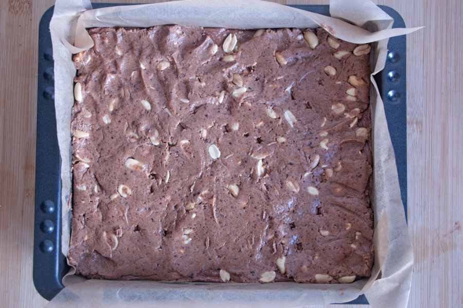 Peanut and protein base layer pressed evenly into a lined baking tin, ready for the chocolate topping.
