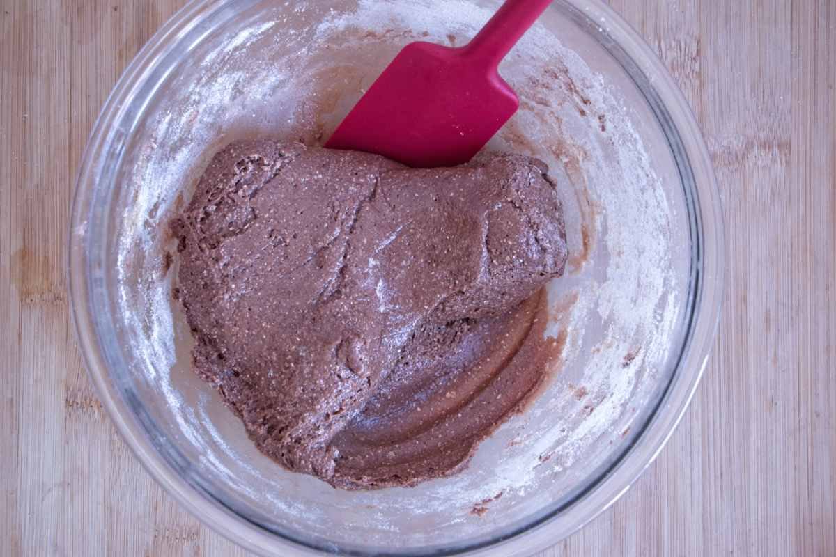 Thick protein and peanut butter nougat mixture being combined in a glass bowl with a spatula before pressing into the tin.