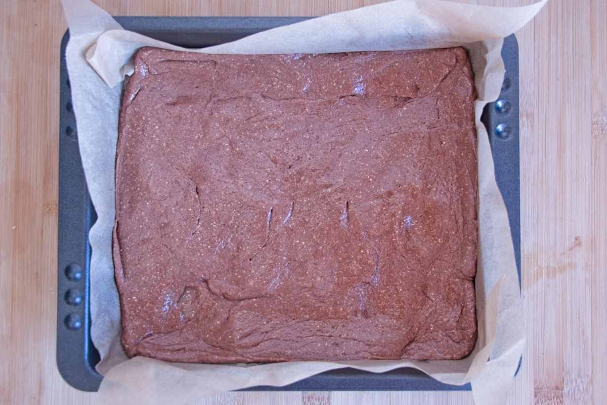 Peanut and protein nougat base pressed evenly into a lined 23 × 23 cm tin before adding the caramel layer.