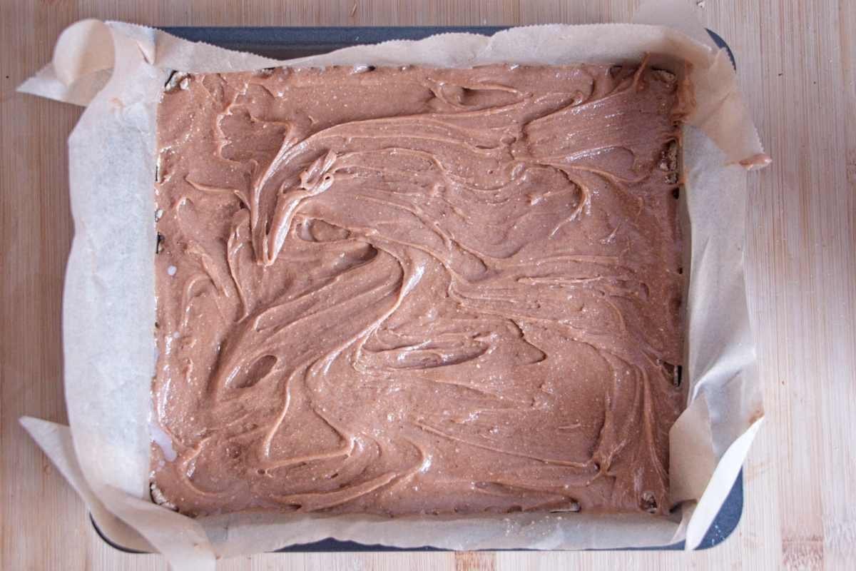 Smooth protein caramel layer spread evenly over a pressed oat base in a lined square tin
