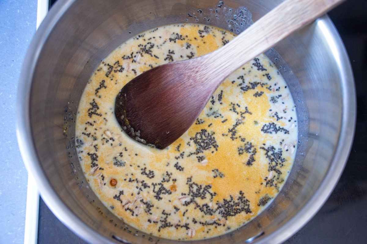 Oats and chia seeds simmering in milk with turmeric in a saucepan, stirred with a wooden spoon.