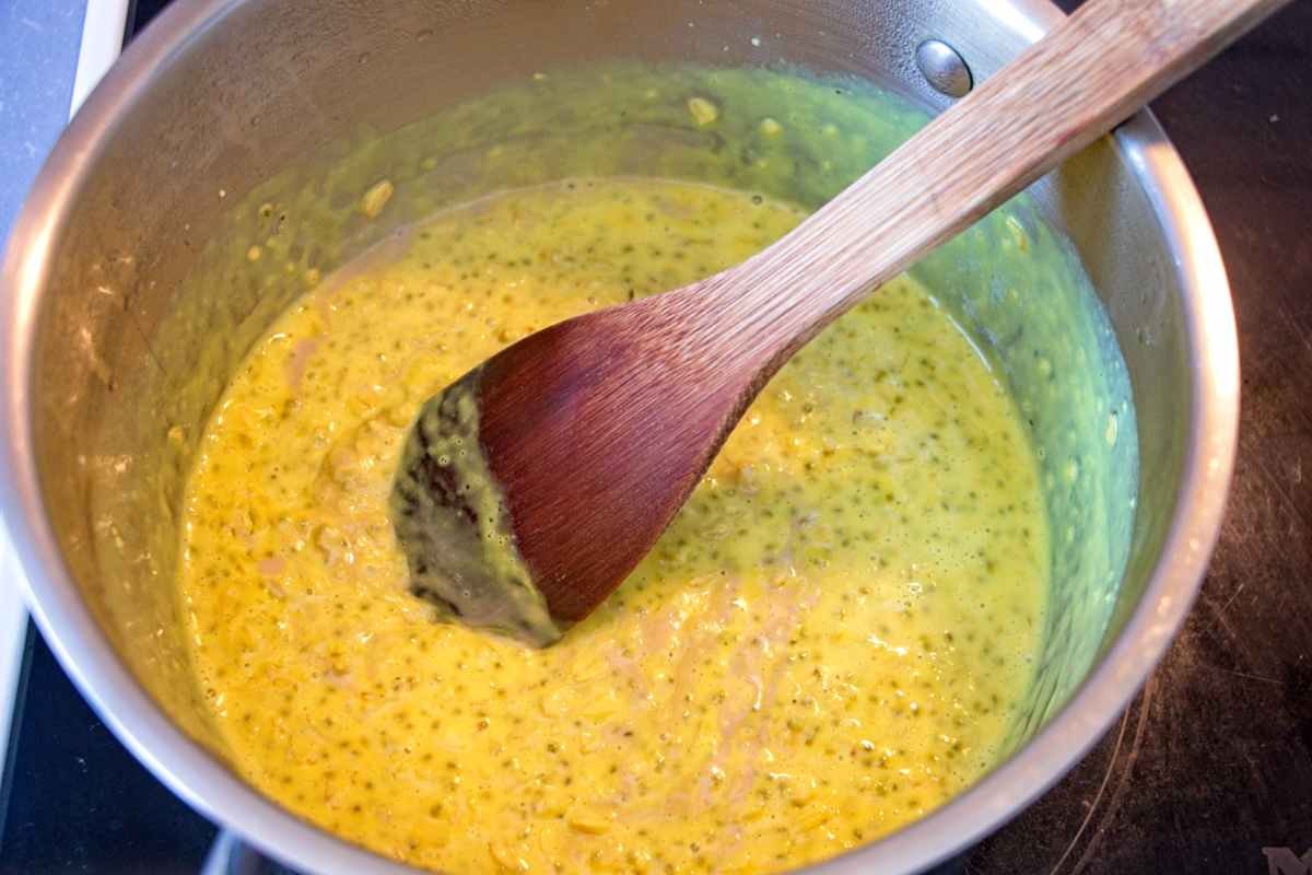 Turmeric oatmeal simmering in a saucepan with chia seeds and cashew butter being stirred with a wooden spoon.