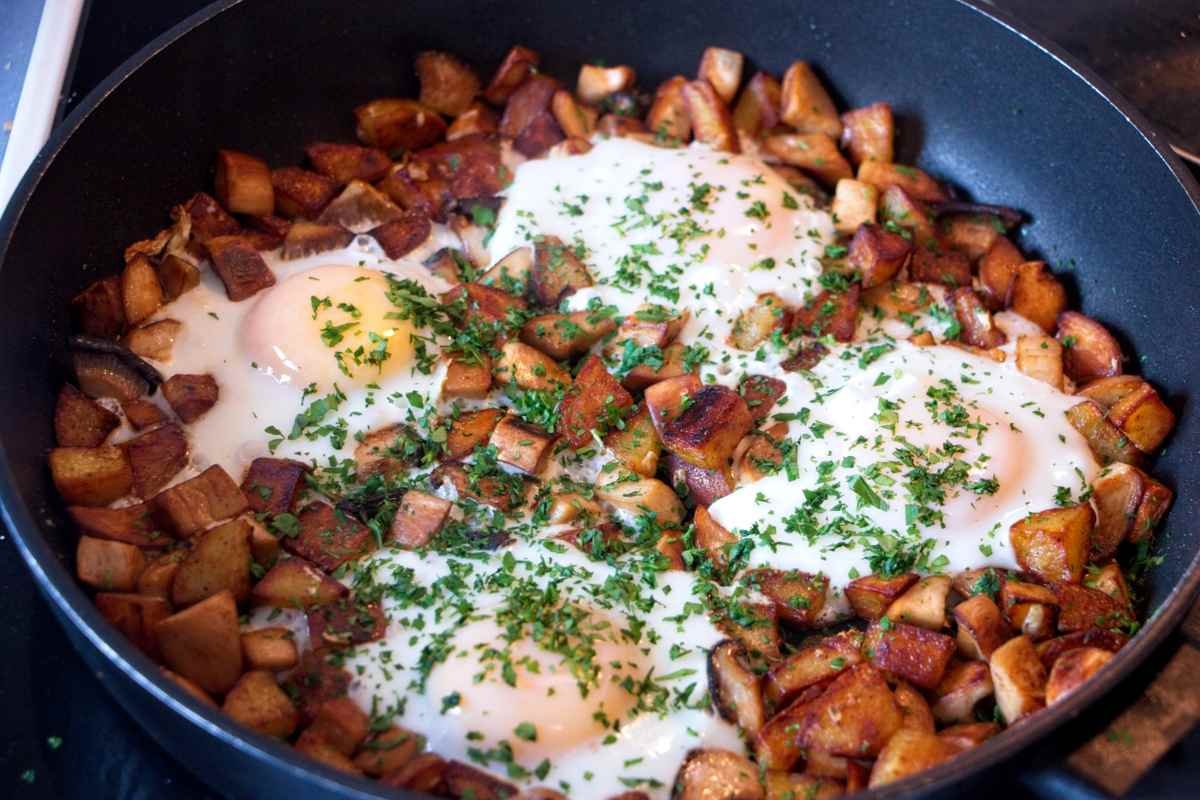King oyster mushroom breakfast hash with crispy potatoes and soft eggs cooked in a skillet, finished with chopped herbs.