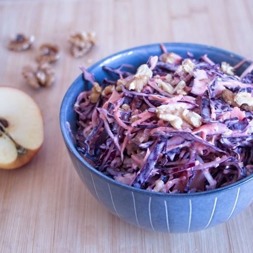 Winter coleslaw with red cabbage, apple, and toasted walnuts in a blue bowl, dressed with Greek yogurt.