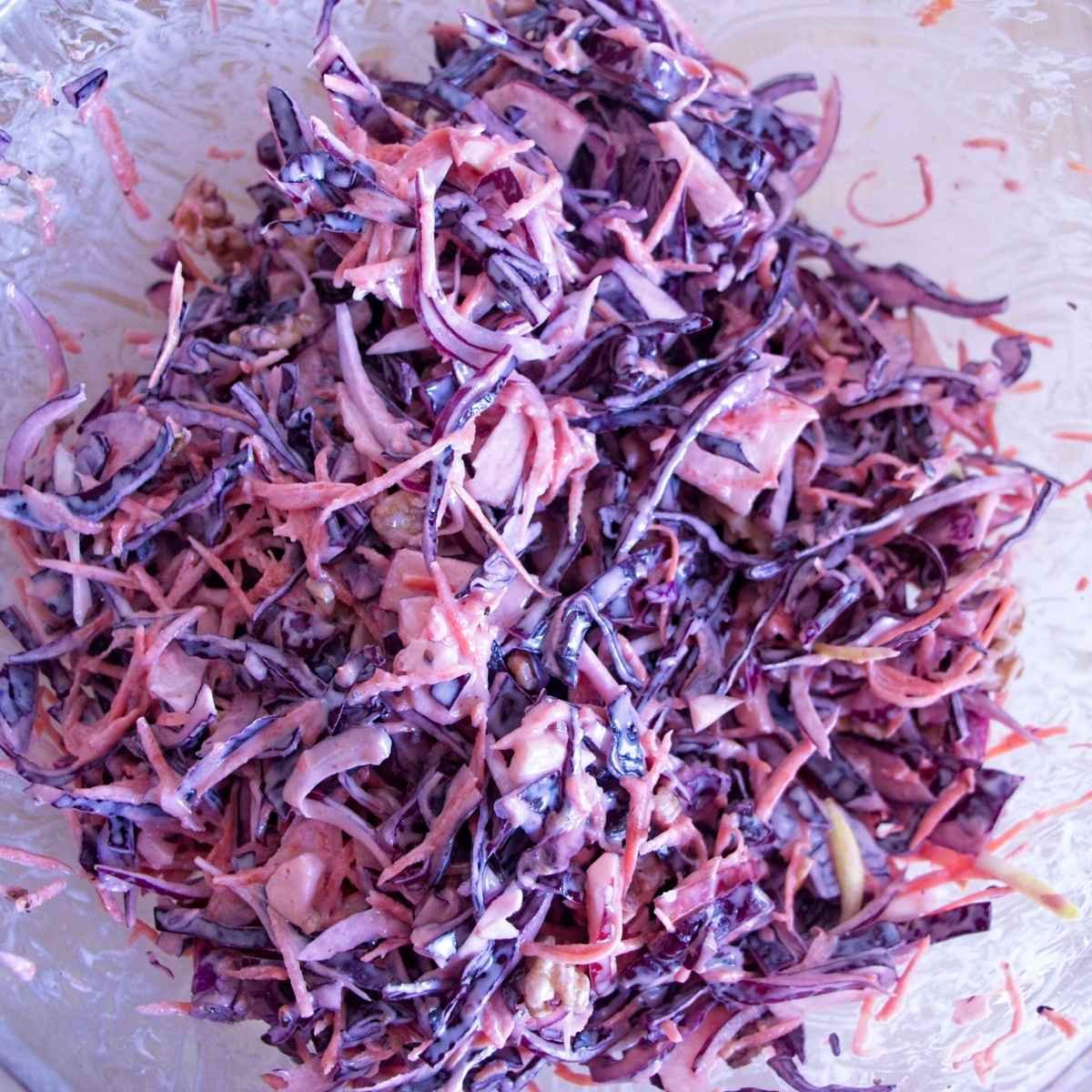 Winter coleslaw mixed in a bowl, showing shredded red cabbage, carrot, apple, and yogurt dressing.