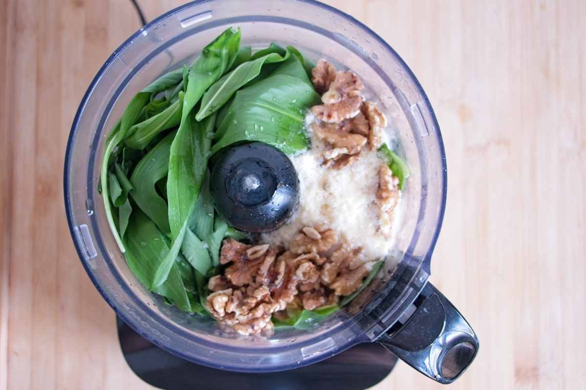 Fresh wild garlic leaves, walnuts, and grated cheese added to a food processor before blending