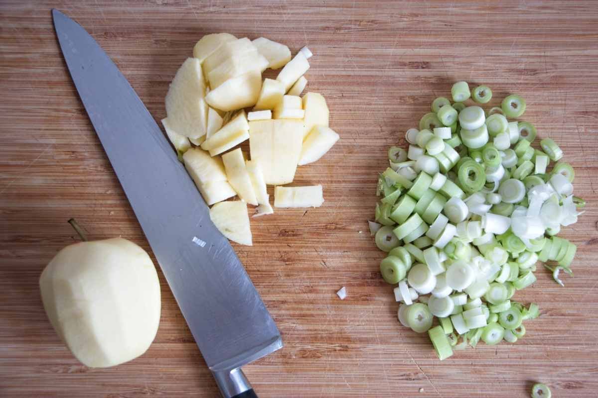 hopping apples and spring onions on a wooden cutting board with kitchen knife
