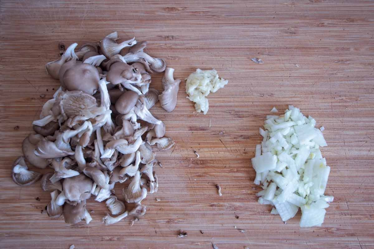 chopped oyster mushrooms, diced onion, and minced garlic on a wooden cutting board ready for cooking