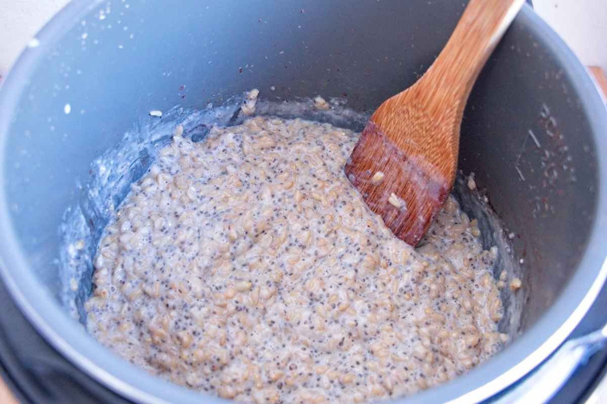 instant pot oat groats cooked into porridge and stirred inside the pressure cooker with a wooden spoon