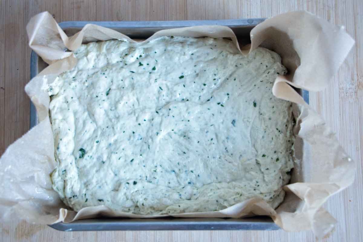 Focaccia dough spread in a lined baking tray ready for the second rise