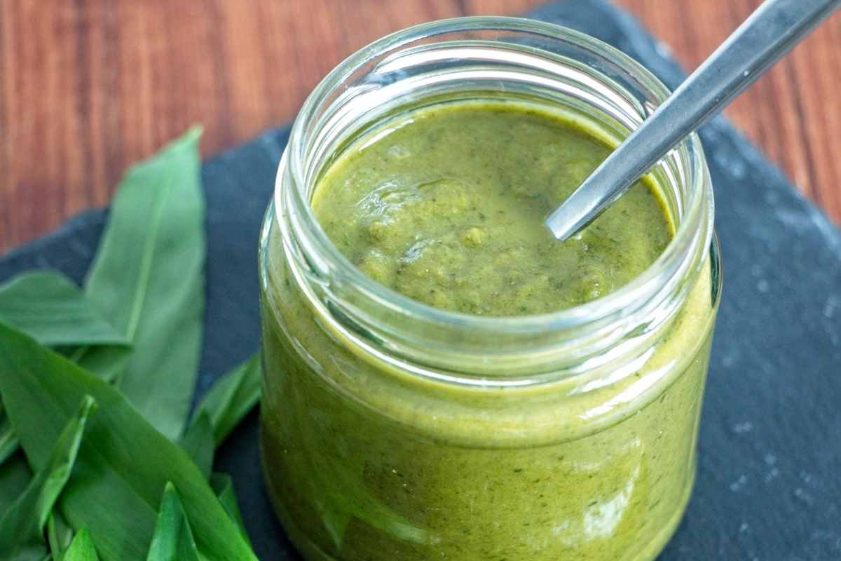 homemade wild garlic ketchup in a glass jar with spoon and fresh ramsons leaves