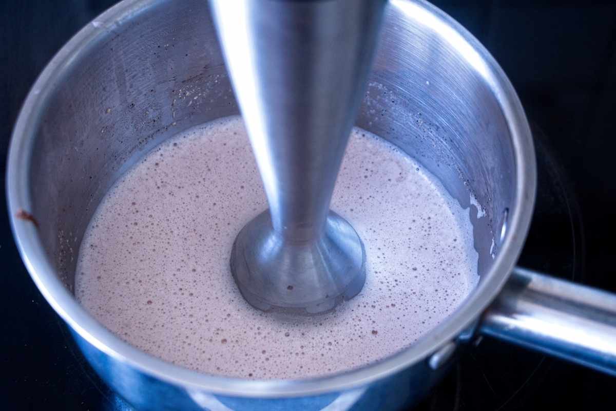 blending warm mushroom latte with stick blender to create smooth, frothy texture