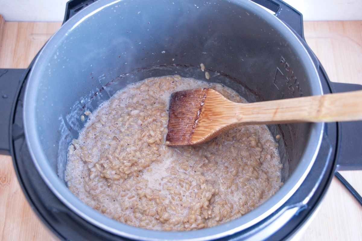 Cooked oat groats being stirred in an electric pressure cooker with a wooden spatula