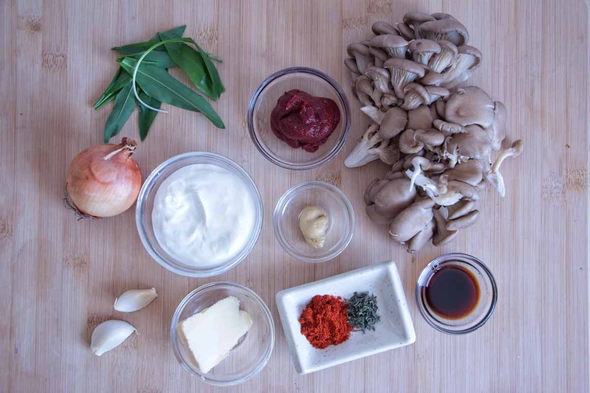 ingredients for slow cooker mushroom stroganoff including oyster mushrooms, onion, garlic, sour cream, paprika, mustard, and tomato paste