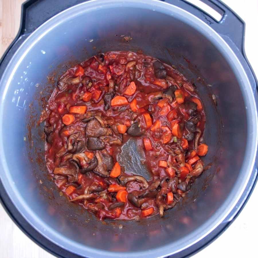 mushrooms, carrots, and tomato base cooking together inside a slow cooker pot