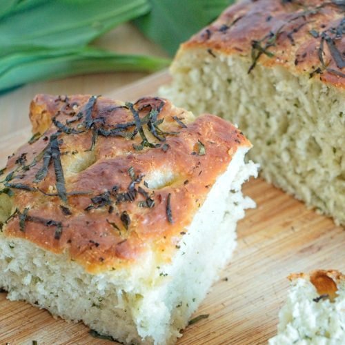 Wild garlic focaccia sliced to show soft airy crumb and golden crust with herbs on top