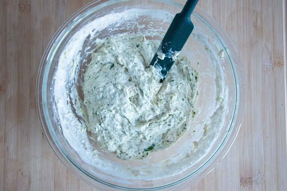 Sticky focaccia dough being mixed in a bowl with visible wild garlic pieces throughout
