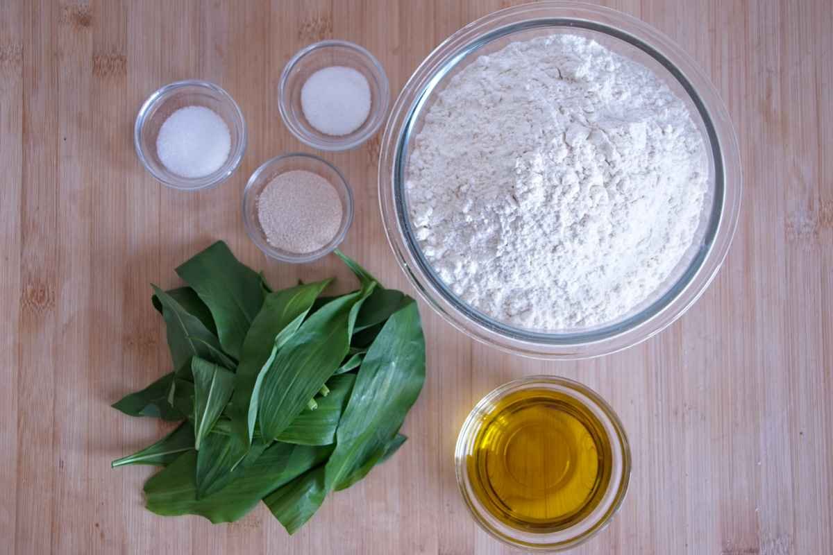 Wild garlic focaccia ingredients including flour, yeast, olive oil, salt, sugar, and fresh wild garlic leaves