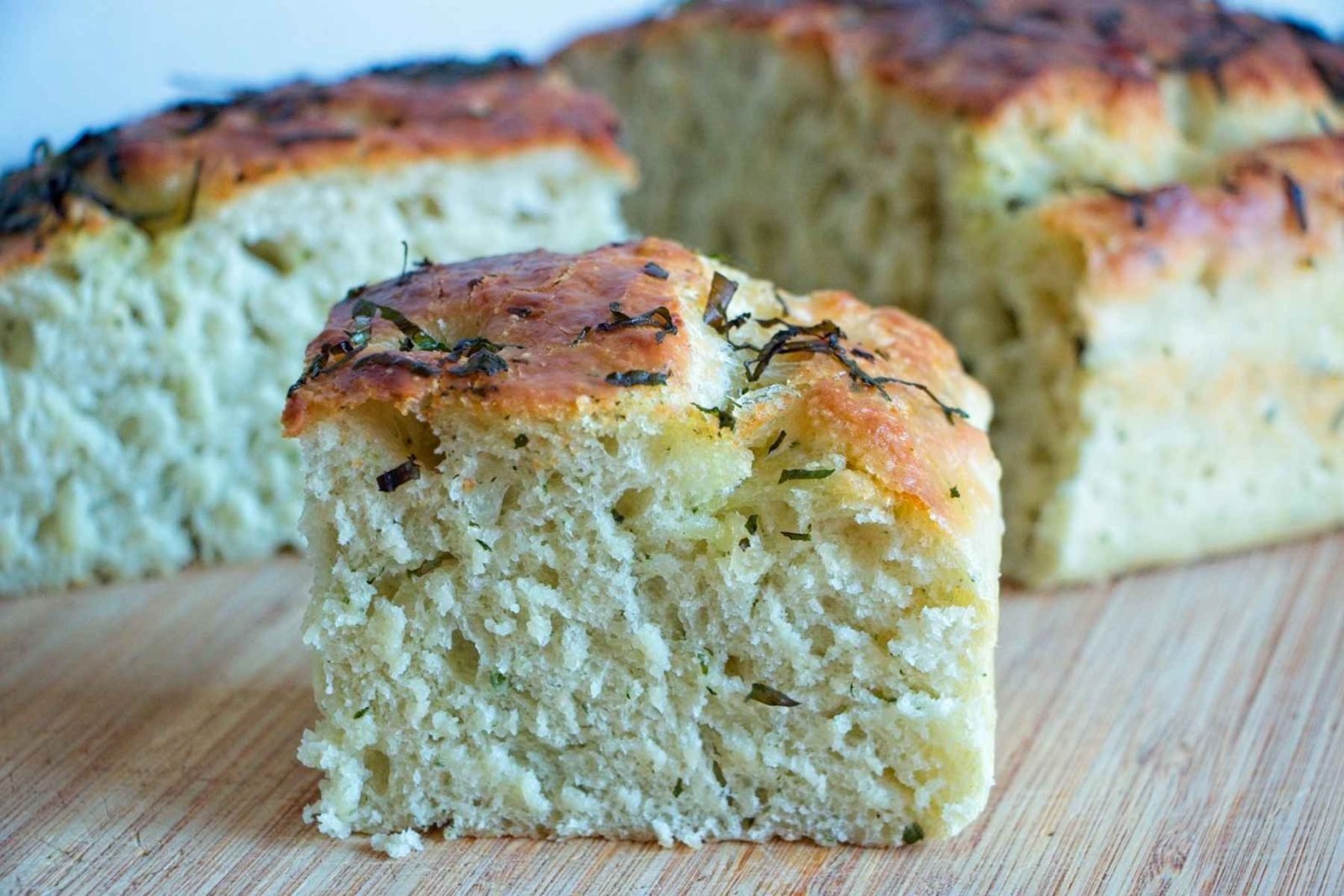 Wild garlic focaccia slice showing soft airy crumb and golden crust with herbs on top