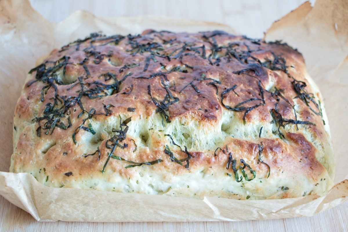 Wild garlic focaccia with golden crust, deep dimples, and scattered wild garlic leaves on top
