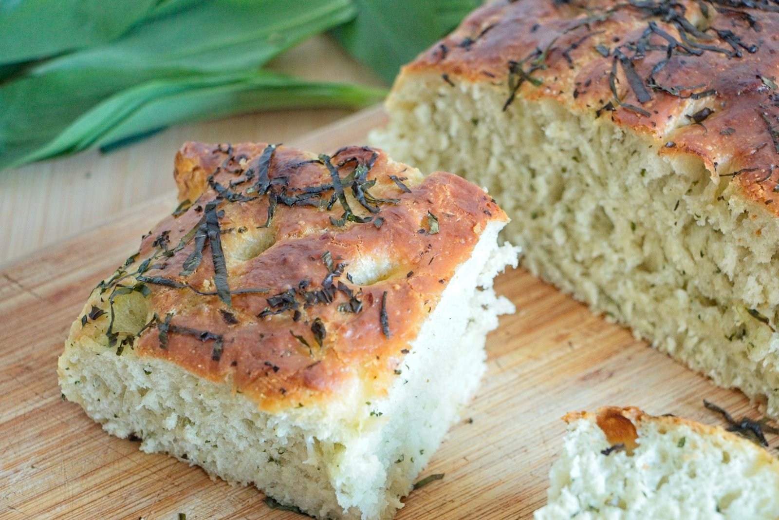 Wild garlic focaccia sliced to show soft airy crumb and golden crust with herbs on top