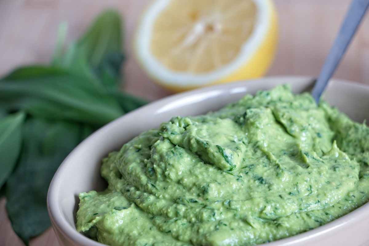 wild garlic hummus close-up showing smooth green texture in bowl with lemon in background