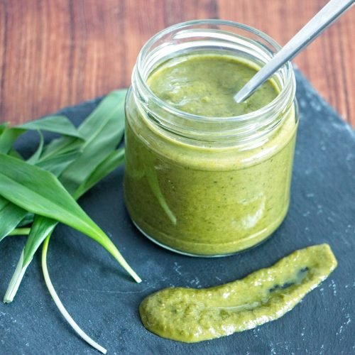 wild garlic ketchup in a glass jar with fresh ramsons leaves on a slate board