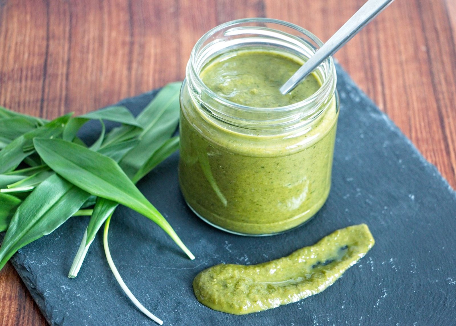 wild garlic ketchup in a glass jar with fresh ramsons leaves on a slate board